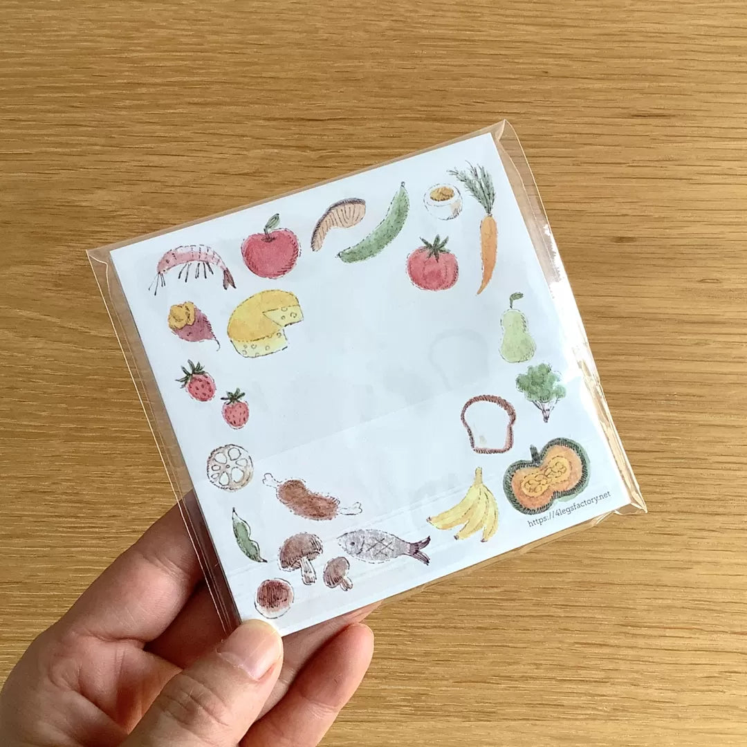 Small notebook with food-themed illustrations held by a hand on a wooden surface