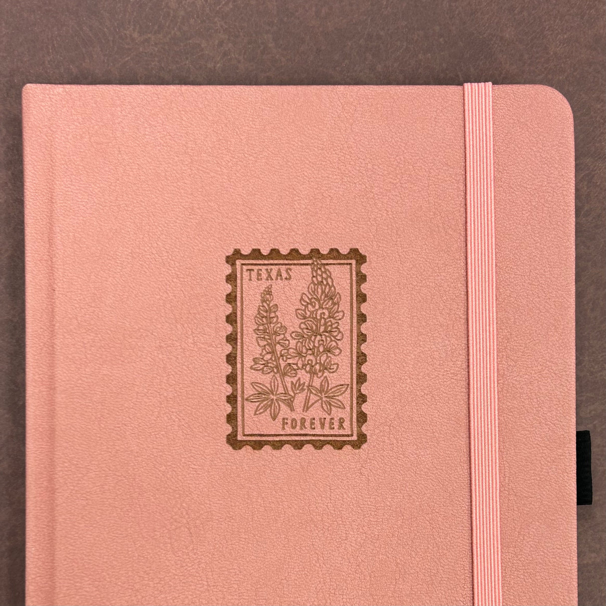 Archer and Olive A5 Notebook - Texas Forever
A charming pink journal featuring a Texas bluebonnet forever stamp on the cover — a sweet nod to the Lone Star State and a perfect keepsake for writers, travelers, and stationery lovers.
✨ Features You’ll Love
Ultra-thick paper designed to prevent ghosting and bleeding
Elastic closure to keep pages secure
Built-in pen loop for your favorite pen or pencil
📓 Notebook Details
Size: A5
Pages: 118 pages
Paper: 160gsm ultra-thick, bleed-resist