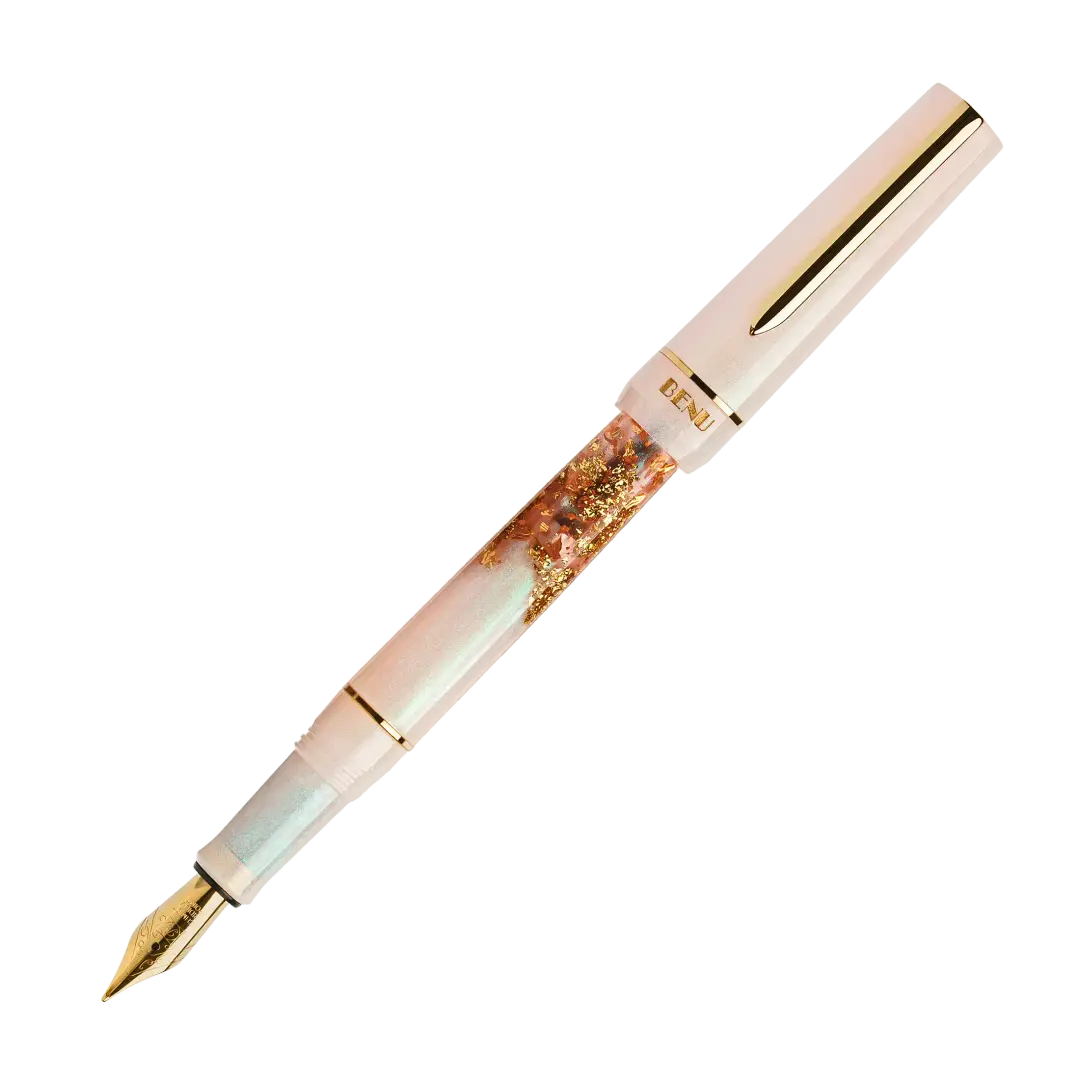 BENU presents the newest Haute Collection — a line of elegant, fashion-inspired pens that blend classic charm with bold, modern flair. The designs include both subtle and vibrant styles, showcasing BENU’s signature glitter and color artistry. Each pen features a faceted body with alternating wide and slender facets, complemented by either gold-plated or chrome-plated trims for a sleek, timeless look.
A mix of golden flakes dances through a soft, pearly pink base, complemented by gleaming gold trim. Tender