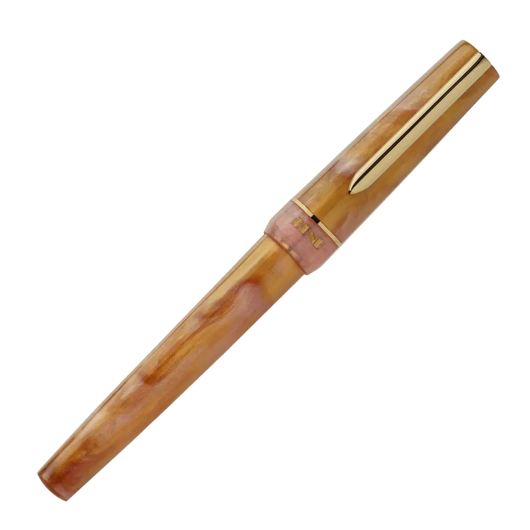 BENU presents the newest Haute Collection — a line of elegant, fashion-inspired pens that blend classic charm with bold, modern flair. The designs include both subtle and vibrant styles, showcasing BENU’s signature glitter and color artistry. Each pen features a faceted body with alternating wide and slender facets, complemented by either gold-plated or chrome-plated trims for a sleek, timeless look.
Lustre pen glows with warm swirls of amber and blush, finished in radiant gold trim.Quietly luxurious, Lust