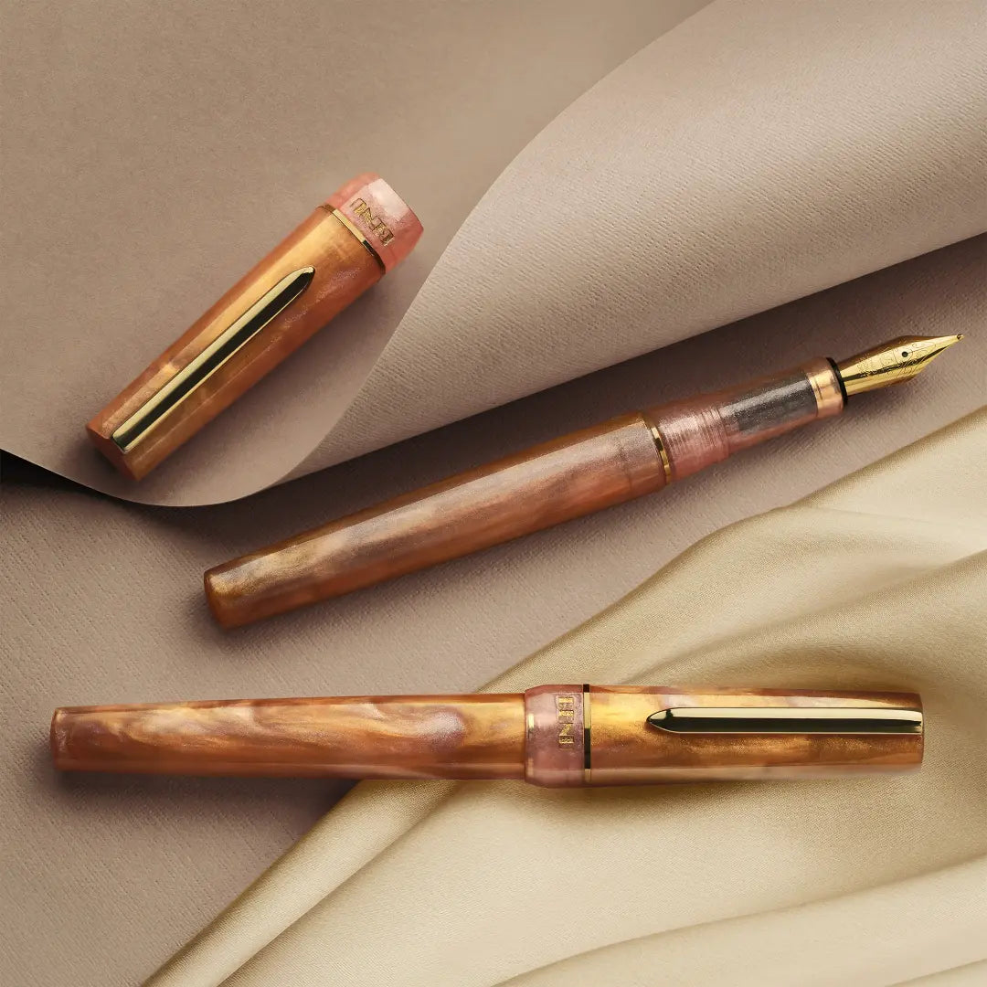BENU presents the newest Haute Collection — a line of elegant, fashion-inspired pens that blend classic charm with bold, modern flair. The designs include both subtle and vibrant styles, showcasing BENU’s signature glitter and color artistry. Each pen features a faceted body with alternating wide and slender facets, complemented by either gold-plated or chrome-plated trims for a sleek, timeless look.
Lustre pen glows with warm swirls of amber and blush, finished in radiant gold trim.Quietly luxurious, Lust