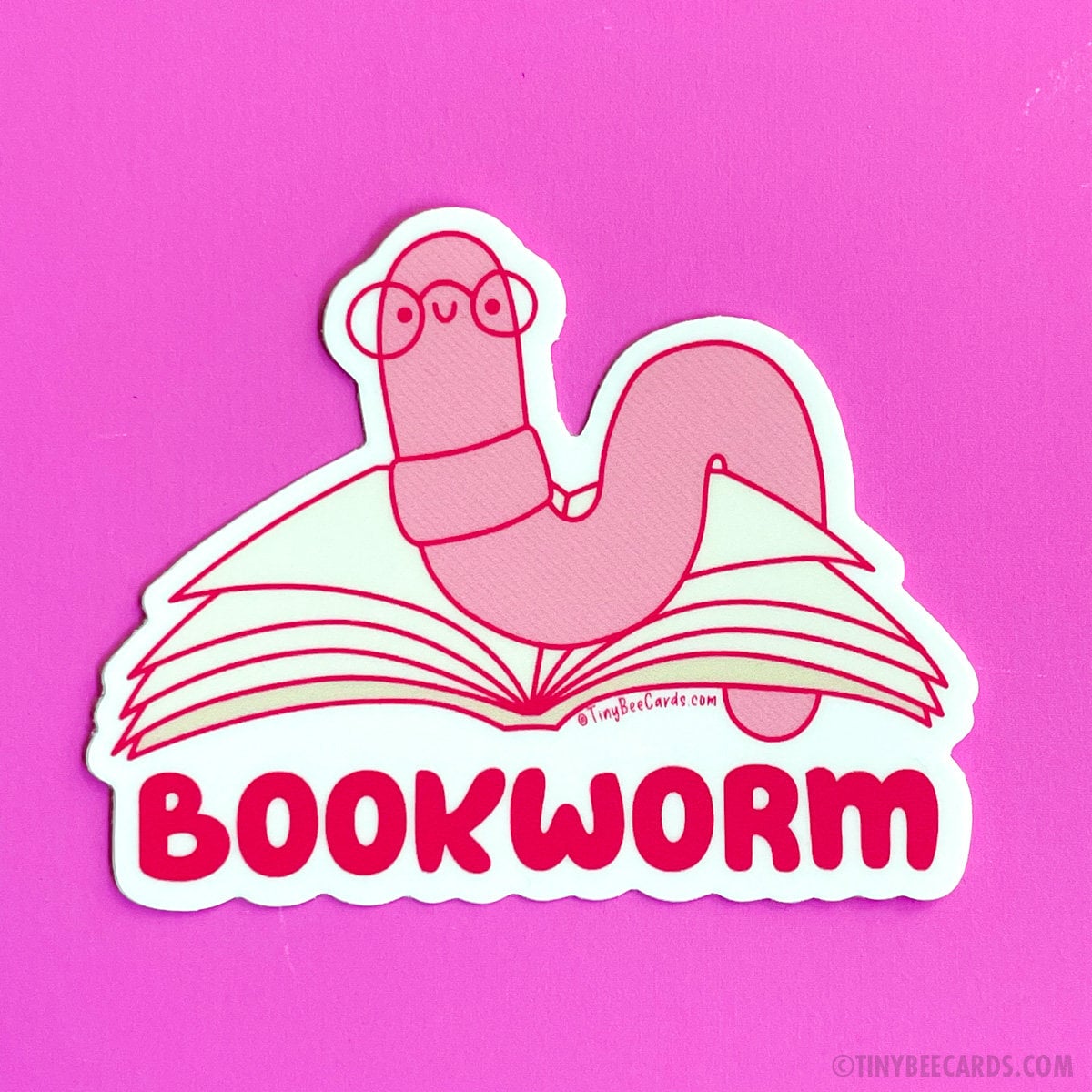 The bookworm is a truly unique creature. This cute little worm spends its days burrowing through the pages of many books and with its tiny glasses it wiggles its way through the literary landscape, reading tales of adventure, love, and knowledge. It immerses itself in the tapestry of stories, traveling through realms of imagination and finds joy in the depths of literature. Celebrate reading with this cute little wormie if that sounds like you too! Design features a hand drawn worm reading a book with the w