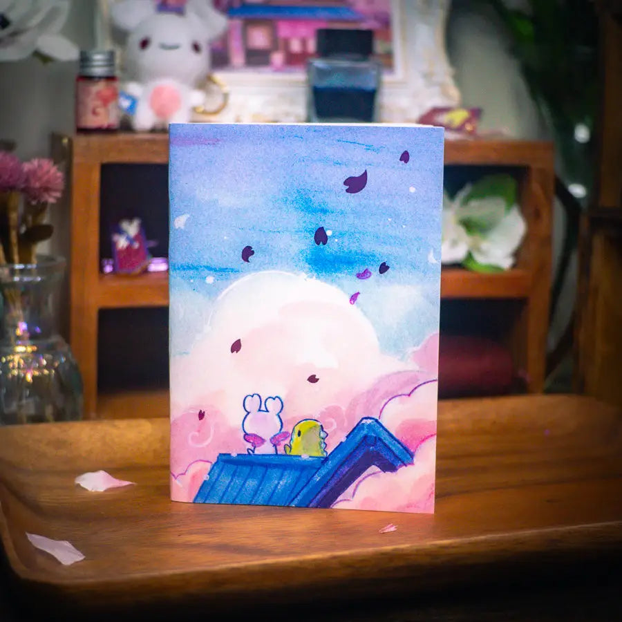 Esterbrook x Sakuradragon - Sakura Street Morning Skies A6 Notebook
Mornings are quiet around here.
Did you notice the pink foil cherry blossoms falling from the sky?
Dimensions: A6 (10.5 × 14.8 cm)
Paper: Double-sided offset paper
Page Ruling: Blank
Pages: 64
Message from sakuradragon: Not all paper and ink are made equal but this paper does a great job with both fountain pens and dip pens. There is minimal ghosting but bleeding does occur with heavy ink usage.