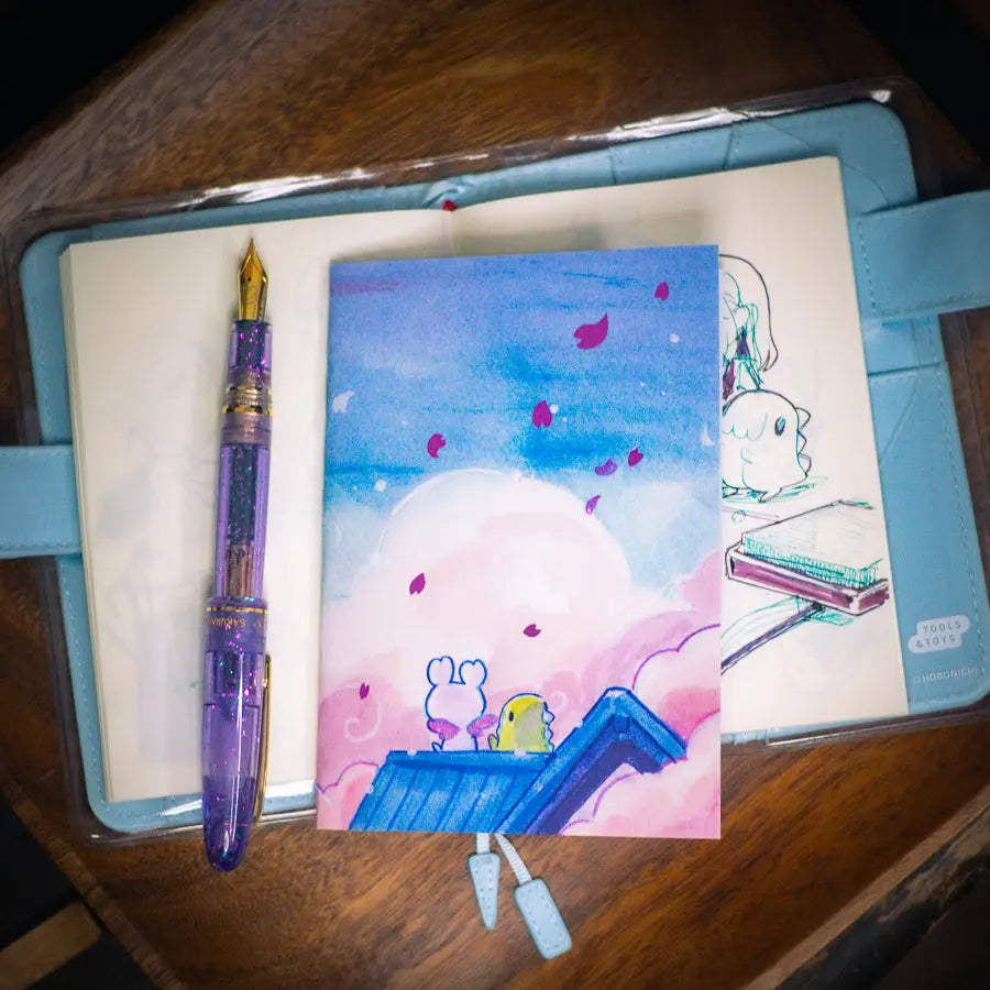 Esterbrook x Sakuradragon - Sakura Street Morning Skies A6 Notebook
Mornings are quiet around here.
Did you notice the pink foil cherry blossoms falling from the sky?
Dimensions: A6 (10.5 × 14.8 cm)
Paper: Double-sided offset paper
Page Ruling: Blank
Pages: 64
Message from sakuradragon: Not all paper and ink are made equal but this paper does a great job with both fountain pens and dip pens. There is minimal ghosting but bleeding does occur with heavy ink usage.