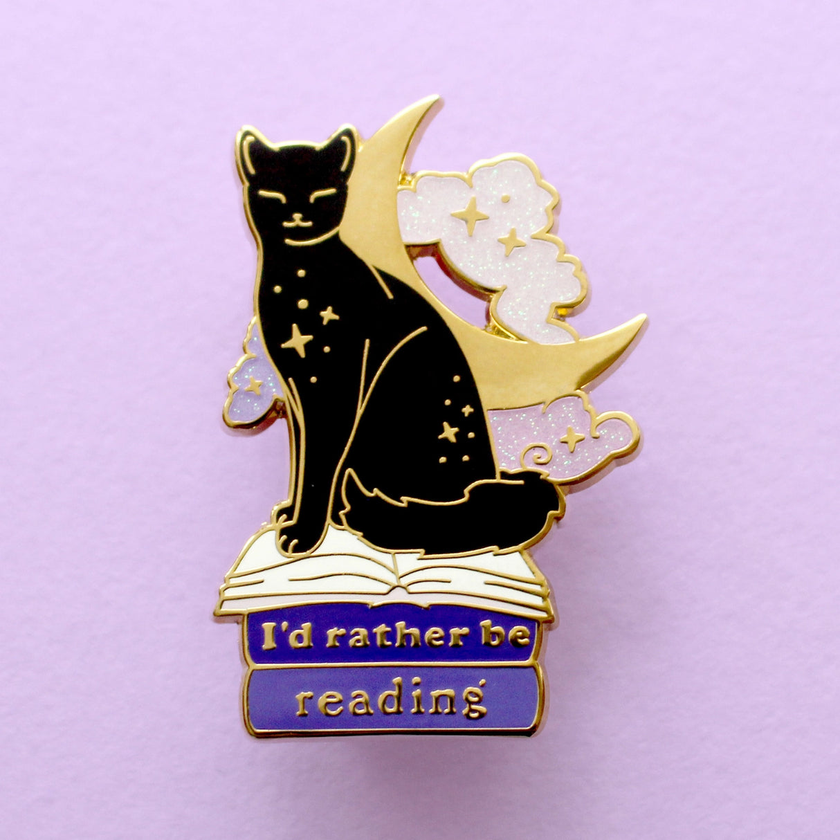 We’ve all sometimes wished we were at home with a hood book, rather than having to deal with the real world! This super cute pin features a black cat sitting on pink & purple books with the slogan ‘I’d rather be reading’. Behind the cat is a large crescent moon and a pair of glittery pastel clouds.
Measurements: 45mm (1.77”)