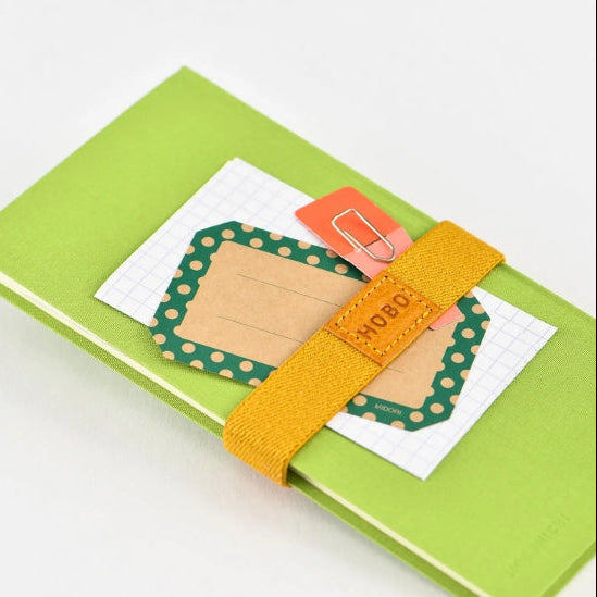 Handy for keeping your book shut in your bag, this bookband is made with an elastic band adorned with the Hobonichi “Hobo” logo. There are two different holes to fit the clasp so you can still use it if your book becomes thicker.
Included in the bookband are slots to store two pens, and the bands come in six colors. (Classic uses natural leather and will grow darker over continued use.)