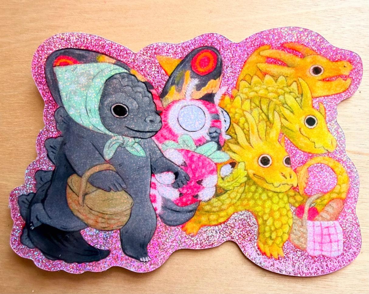 Three Kaiju friends go for a picnic.
This vinyl glittery sticker is weather and waterproof-stick it on a notebook, bike, or car- it's going to stick around! Heck, throw it on a water bottle and through the dishwasher. This sticker can go anywhere. Sticker measures 3.25" x 4.5" Printed in USA.