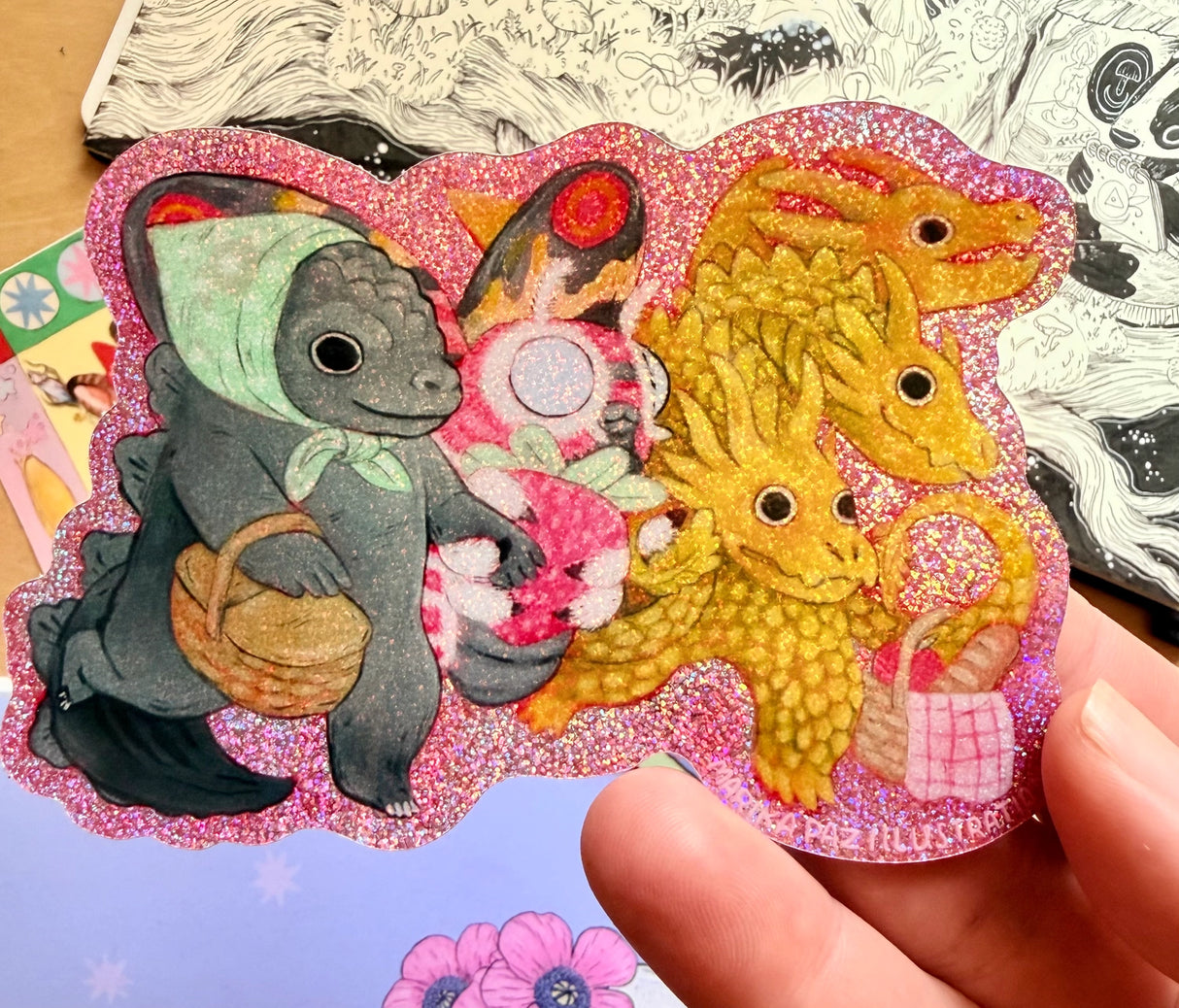 Three Kaiju friends go for a picnic.
This vinyl glittery sticker is weather and waterproof-stick it on a notebook, bike, or car- it's going to stick around! Heck, throw it on a water bottle and through the dishwasher. This sticker can go anywhere. Sticker measures 3.25" x 4.5" Printed in USA.