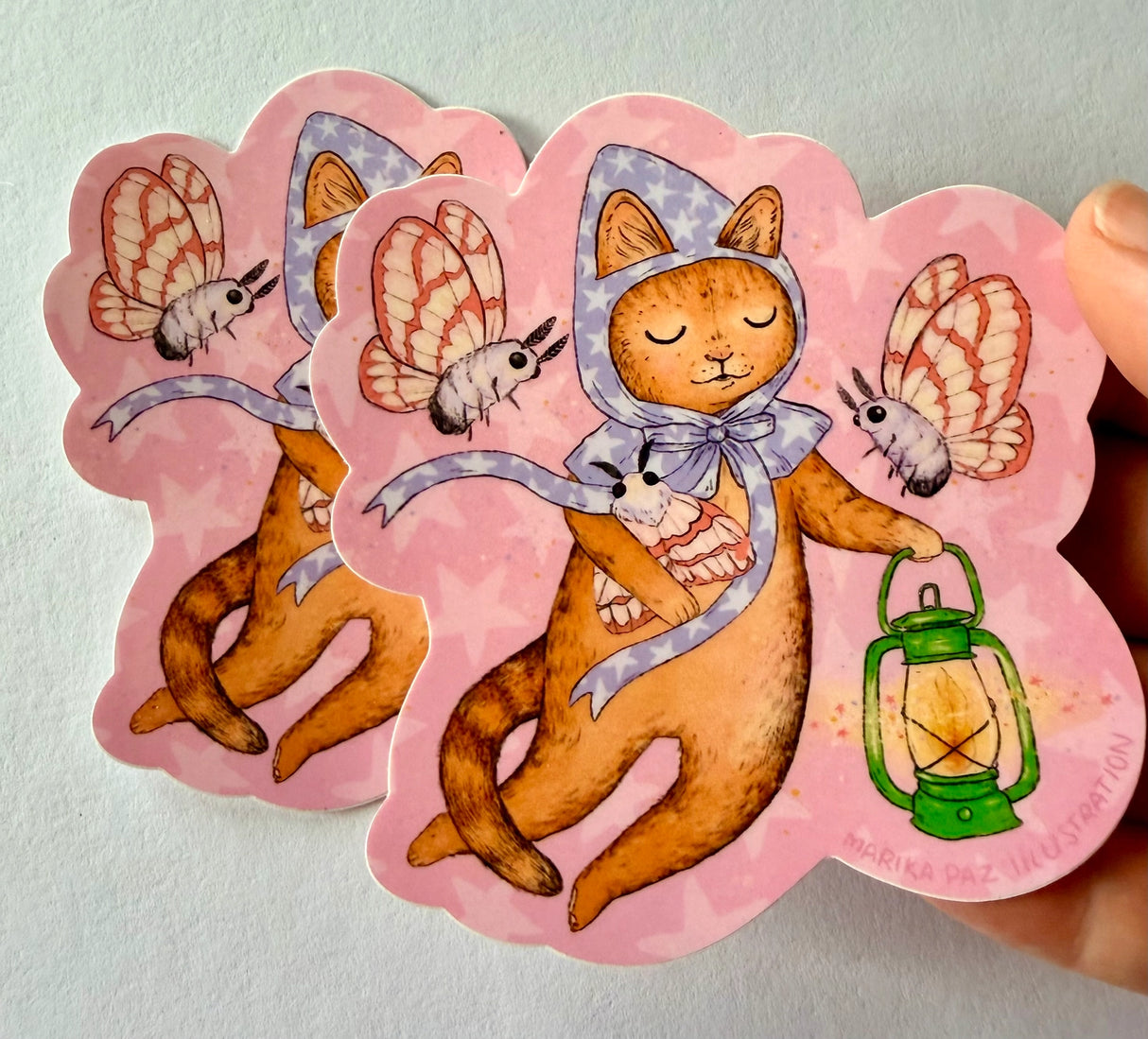 A cat and his lantern attract moths as they float amongst the stars.
This vinyl matte sticker is weather and waterproof-stick it on a notebook, bike, or car- it's going to stick around! Heck, throw it on a water bottle and through the dishwasher. This sticker can go anywhere. Sticker measures 3.5" x 4.5" Printed in USA.