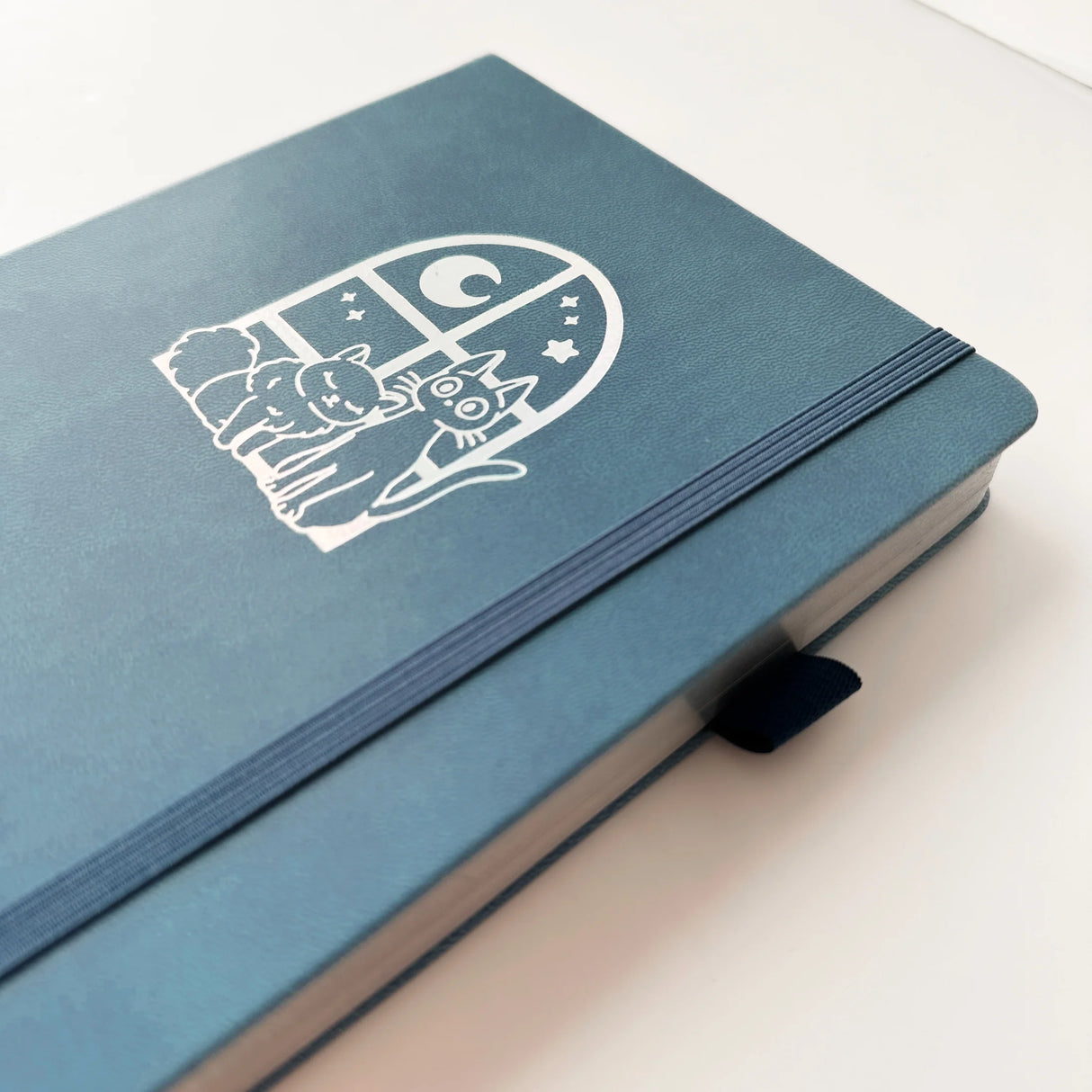 Jiji The Cat Journal in Ocean Blue with Holographic Edges and Logo 🌊✨
Product Details:
Size: A5 (5.70 x 8.26 inches)
160 Dotted Grid Pages (5 x 5 mm)
2 Bookmarks
Elastic Band and Pen Holder
Expandable storage compartment