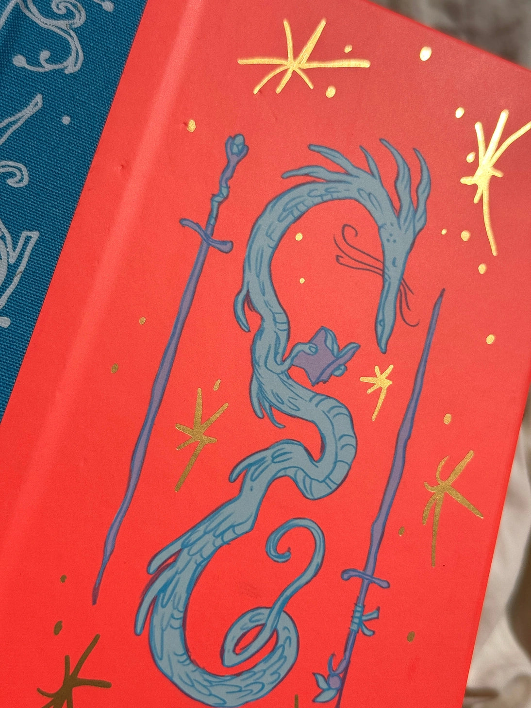 This is a blank 200 page notebook/sketchbook with thin ivory Munken paper perfect for light sketching or writing. Part of a fantasy collection called Woodfolk.
The cover is fluorescent pink/orange and has a smooth matte finish with gold foiling on the front and back. Plus it has a blue fabric spine with white embossing, adding to the charm of the book. Best for pencils, light pens, and generally light mediums, as thick markers or water can bleed. Not recommended for gouache or heavy marker use.