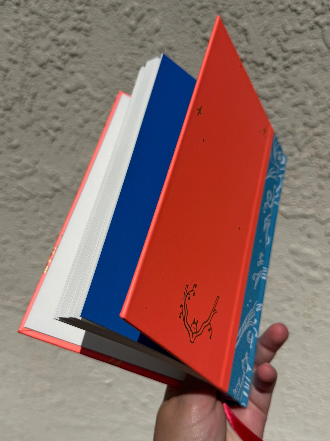 This is a blank 200 page notebook/sketchbook with thin ivory Munken paper perfect for light sketching or writing. Part of a fantasy collection called Woodfolk.
The cover is fluorescent pink/orange and has a smooth matte finish with gold foiling on the front and back. Plus it has a blue fabric spine with white embossing, adding to the charm of the book. Best for pencils, light pens, and generally light mediums, as thick markers or water can bleed. Not recommended for gouache or heavy marker use.