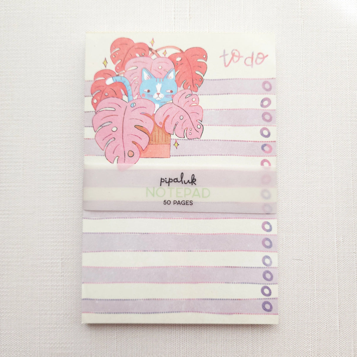 Inside a cozy Wildflower Woods cottage, a curious cat lounges among broad monstera leaves, tucked into a corner filled with filtered light and trailing greenery. This notepad brings that leafy, lived-in moment to your desk, making everyday lists feel a little more inviting.
Designed to be practical without feeling busy, this notepad offers a simple, cheerful way to keep track of daily to-do lists and planning.