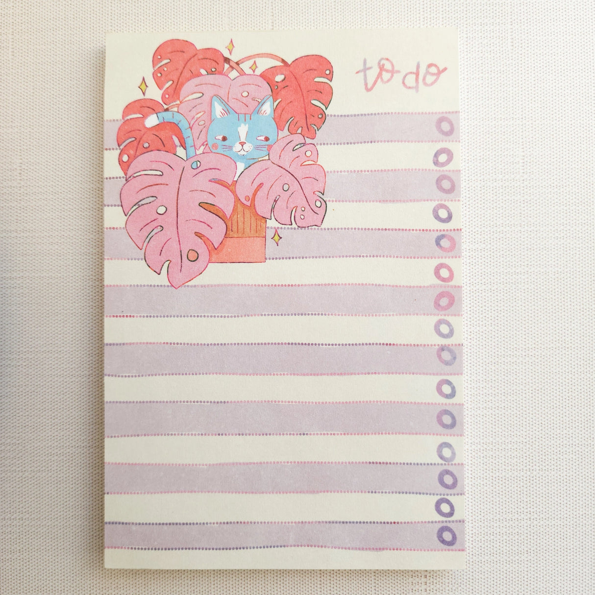 Inside a cozy Wildflower Woods cottage, a curious cat lounges among broad monstera leaves, tucked into a corner filled with filtered light and trailing greenery. This notepad brings that leafy, lived-in moment to your desk, making everyday lists feel a little more inviting.
Designed to be practical without feeling busy, this notepad offers a simple, cheerful way to keep track of daily to-do lists and planning.