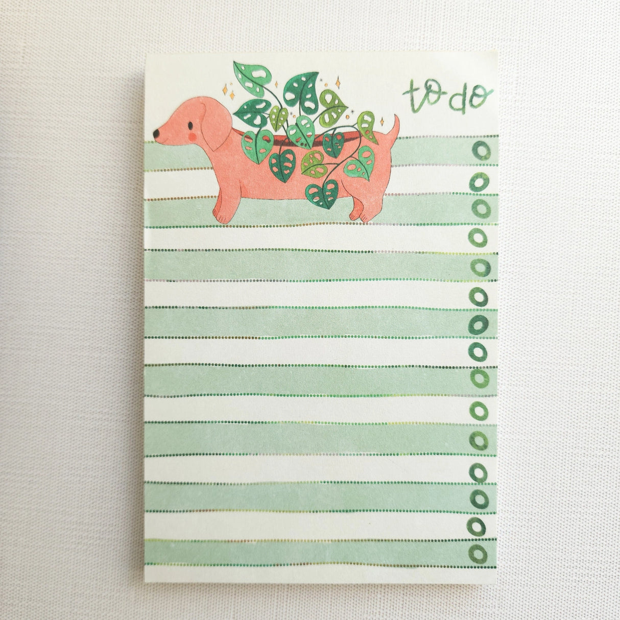 In a sunny Wildflower Woods cottage, a dachshund planter rests near a stack of well-loved books, leafy greens spilling gently from its back. This notepad brings that cozy, decorative moment to your desk, making everyday lists feel a little more inviting.
Designed to be practical without feeling busy, this notepad offers a simple, cheerful way to keep track of daily to-do lists and planning.