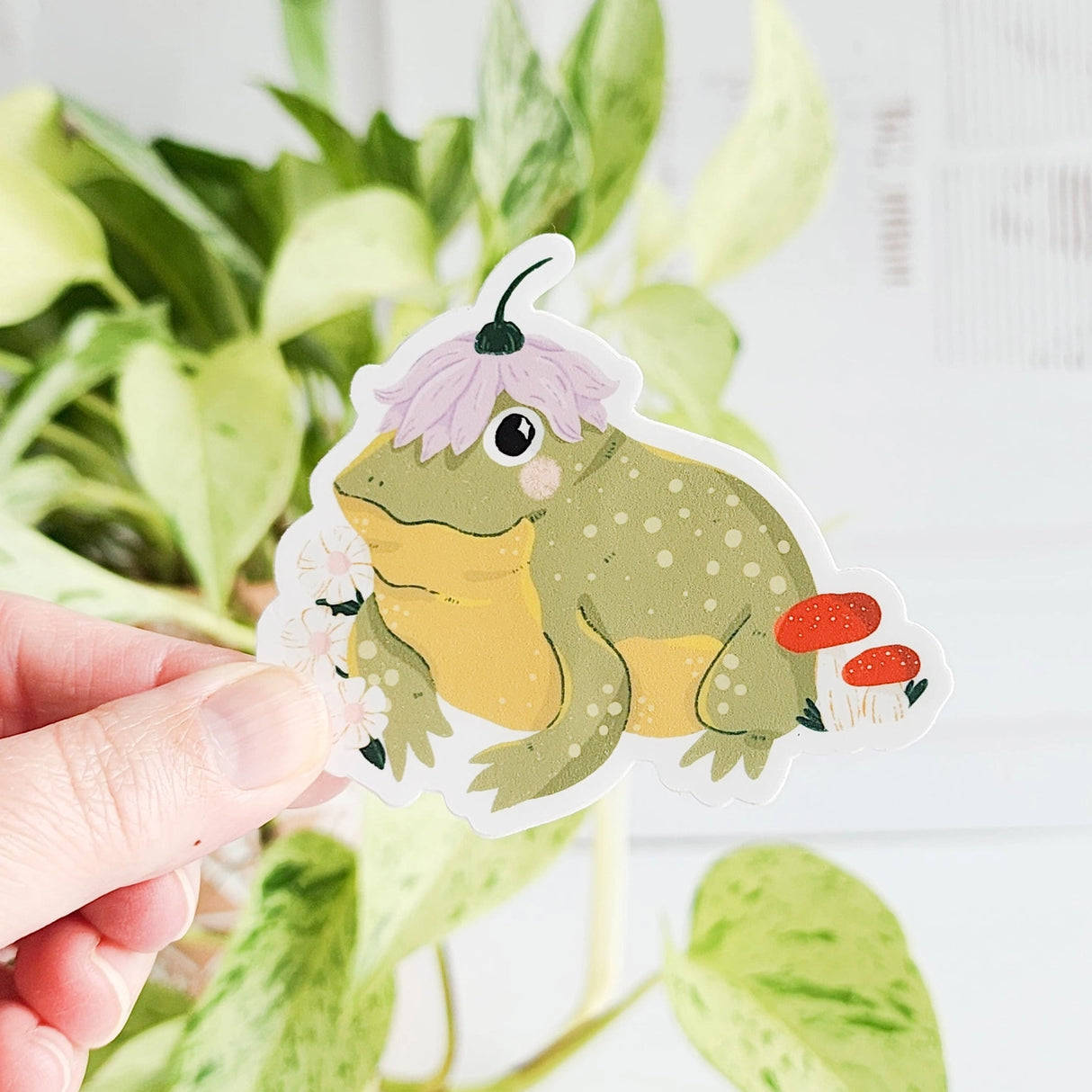 A happy little toad pauses among blooming flowers and mushrooms, a small flower worn proudly atop his head. This vinyl sticker captures that lighthearted moment, celebrating comfort, confidence, and being yourself in the everyday.
Made from durable, waterproof vinyl, this sticker is designed to hold up wherever you place it—whether that’s a water bottle, laptop, or journal you reach for daily.