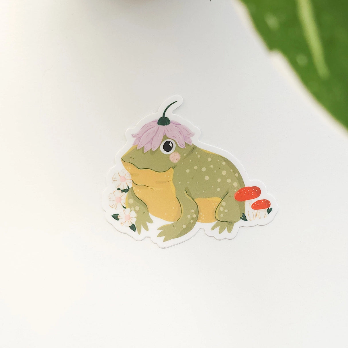 A happy little toad pauses among blooming flowers and mushrooms, a small flower worn proudly atop his head. This vinyl sticker captures that lighthearted moment, celebrating comfort, confidence, and being yourself in the everyday.
Made from durable, waterproof vinyl, this sticker is designed to hold up wherever you place it—whether that’s a water bottle, laptop, or journal you reach for daily.