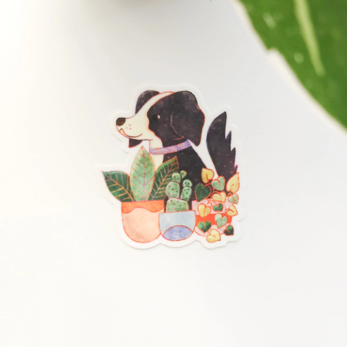 A loyal dog settles in among leafy houseplants, content to rest where sunlight filters softly through the greenery. This vinyl sticker captures that familiar, cozy moment, adding a quiet sense of companionship to your everyday essentials.
Made from durable, waterproof vinyl, this sticker is designed to hold up wherever you place it—whether that’s a water bottle, laptop, or journal you reach for daily.