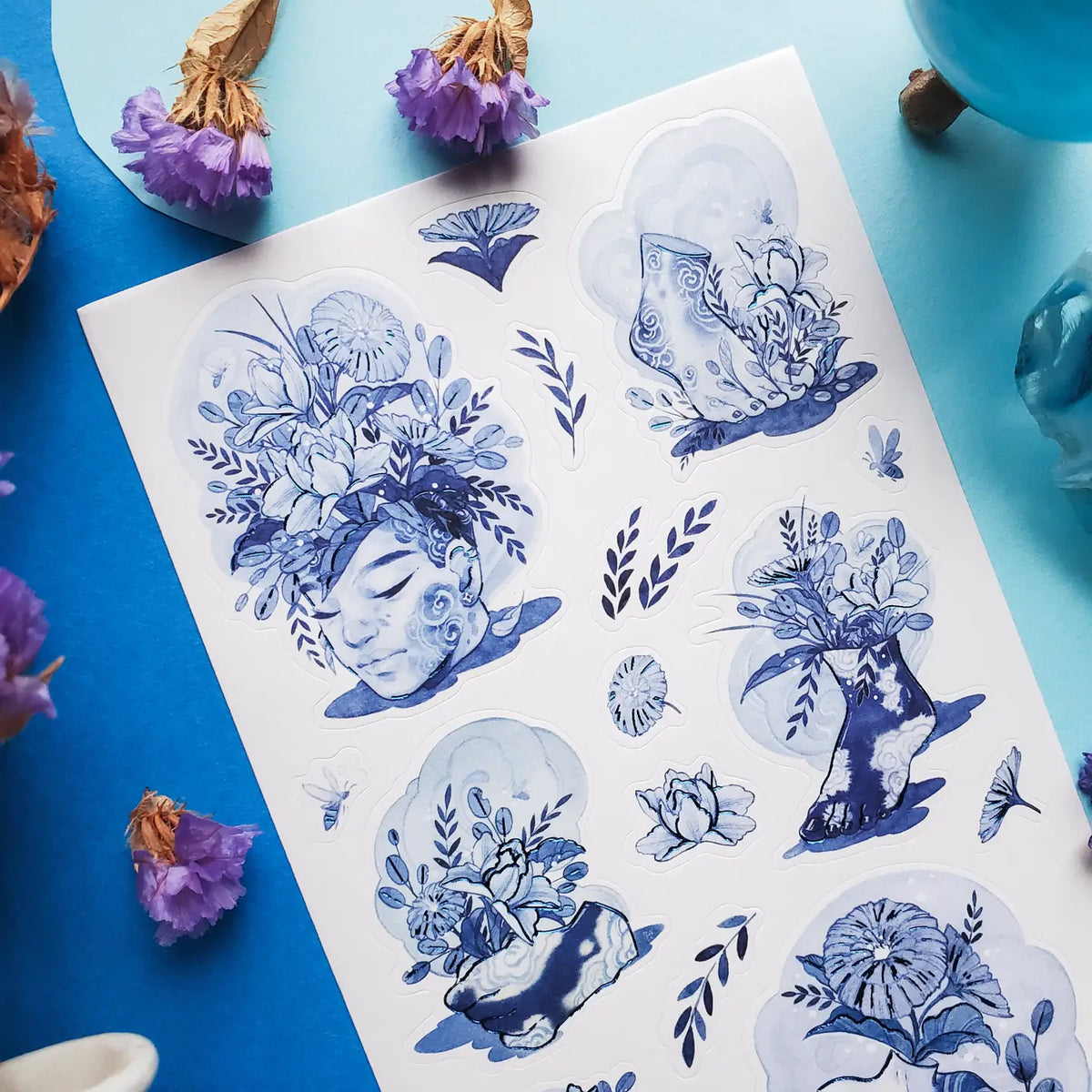 💐🌀 Step into @so.meurdok’s surreal garden, where faces, hands, feet, and figures blossom into living bouquets. Lush florals and striking blue details blur the line between body and bouquet, while foil accents trace every elegant curve like enchanted brushstrokes. A tiny art gallery, now in sticker form. Art by: @so.meurdok
Top Coating: Blue foil
Adhesive Layer: Paper
Backing Layer: Paper
6.69" x 3.54".
Weight - 0.03lbs
1 sheet included