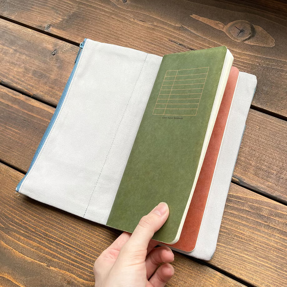 Made of cotton that feels good to the touch, this is RO-BIKI NOTE CANVAS COVER vintage blue. A zippered pocket on the side is useful for storing stationery that tends to be loose. It has a simple design that does not stand out when carrying. When closed, it feels neat and sizable. The surface of the cover has three pockets of different sizes, so you can enjoy multiple storage options.
With a connecting band, you can sandwich the Basic size and the passport size at the same time.