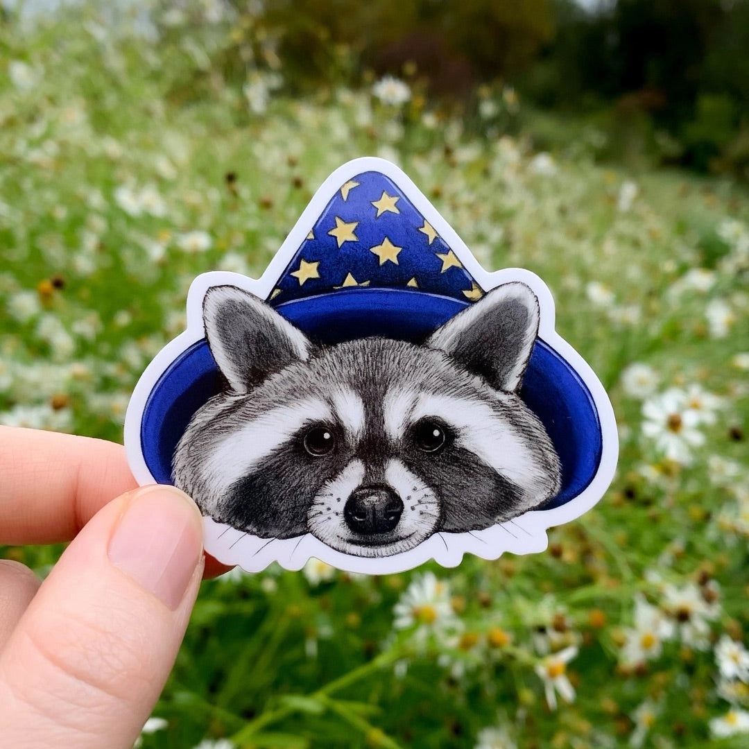 This 2.75” weatherproof vinyl sticker features my illustration of a raccoon wizard wearing a blue hat with gold stars! This die-cut gloss vinyl sticker is durable, weatherproof, and perfect for water bottles, notebooks, laptops, bikes, and all sorts of other surfaces!
Make sure to clean and dry the surface thoroughly before applying.
This opossum wizard sticker is perfect for people who love wildlife, raccoons, whimsy, magic, fall, Halloween, and all things mystical.