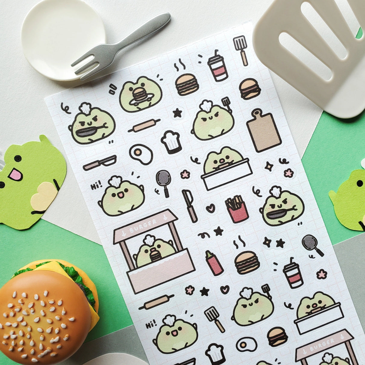 🍔🐸 Say hello to the cutest chef in town! @keziacreations’ adorable little froggy is busy in the kitchen flipping patties and serving up smiles. From sizzling burgers to crispy fries and fizzy drinks, this tiny chef is here to make your heart (and tummy) hoppy.
Art by: @keziacreations
Top Coating: None
Adhesive Layer: Paper
Backing Layer: Clear PET
6.69" x 3.54".
Weight - 0.03lbs.
1 sheet included 