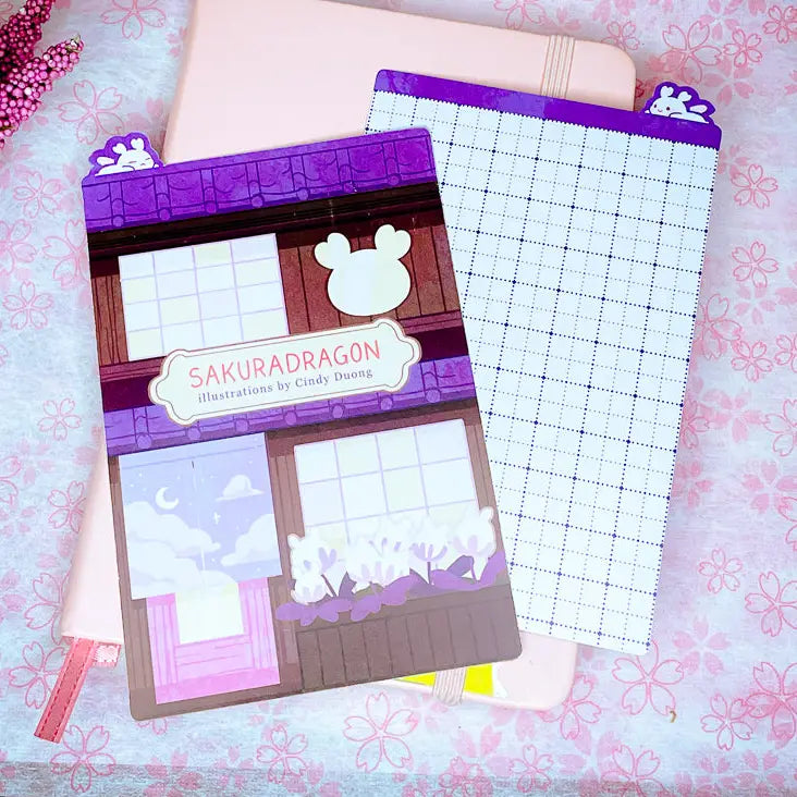 Sakuradragon - Sakura Street A6 Pencil Board
A napping Sakuradragon perched onto of a cozy little shop Sakura Street. It's almost as if she is sleeping on top of your notebook.
What is a pencil board?
Pencil boards are inserts for your notebook that sit under the page you are writing on. They prevent indents on the next page when you write and even prevent ink from bleeding through to the page beneath. But honestly, they can just be cute bookmarks.