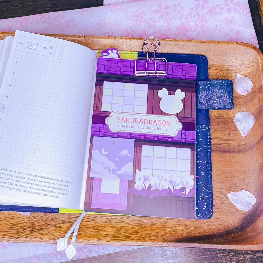 Sakuradragon - Sakura Street A6 Pencil Board
A napping Sakuradragon perched onto of a cozy little shop Sakura Street. It's almost as if she is sleeping on top of your notebook.
What is a pencil board?
Pencil boards are inserts for your notebook that sit under the page you are writing on. They prevent indents on the next page when you write and even prevent ink from bleeding through to the page beneath. But honestly, they can just be cute bookmarks.