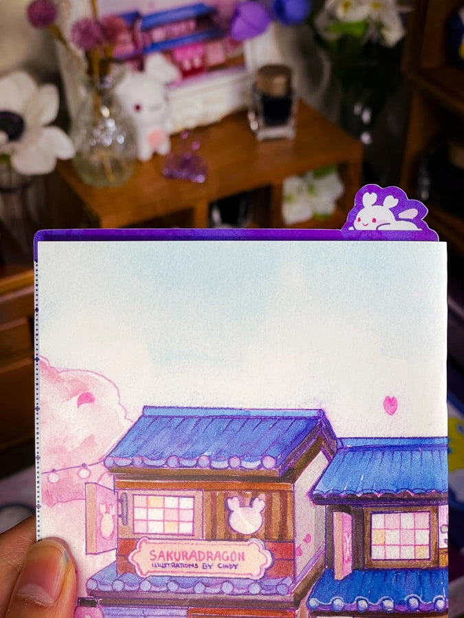 Sakuradragon - Sakura Street A6 Pencil Board
A napping Sakuradragon perched onto of a cozy little shop Sakura Street. It's almost as if she is sleeping on top of your notebook.
What is a pencil board?
Pencil boards are inserts for your notebook that sit under the page you are writing on. They prevent indents on the next page when you write and even prevent ink from bleeding through to the page beneath. But honestly, they can just be cute bookmarks.