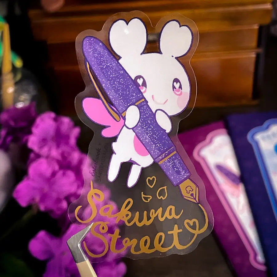 Sakuradragon - Sakura Street Fountain Pen Clear Vinyl Sticker
Sakuradragon really look like she's shining with that pen.
Product Details:
• Material: PET (clear plastic - oil proof, UV resistant, and waterproof)
• Dimensions: 3.5in x 2.37in
• Foil: Gold