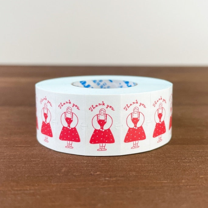 Roll of tape with red illustrations and 'Thank you' text on a wooden surface