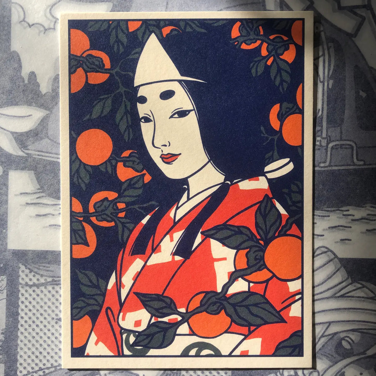 This portrait represents a yūrei (Japanese ghost) wearing a hitaikakushi (white paper triangle) on her forehead. Her makeup and hair are inspired by the style of the Heian period (794-1185). It is surrounded by persimmons, which are a very popular fruit in Japan.
• Postcard size A6 (14.8 × 10.5 cm)
• Old Mill Premium White 300g paper
• Digital printing
• Printed in France