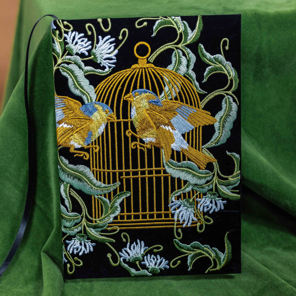Embroidered fabric panel with birds and a cage design on a green background