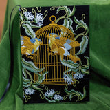 Embroidered fabric panel with birds and a cage design on a green background