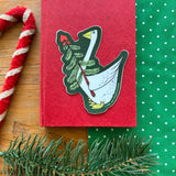 This vinyl sticker features a Petunia® Christmas motif in green tones, proudly made in the U.S.A. from Three Potato Four. Easy to apply to surfaces, it adds a decorative, retro-style touch to gifts and items.