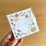 Small notebook with food-themed illustrations held by a hand on a wooden surface