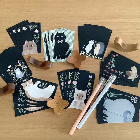 Collection of black cards with cat illustrations on a wooden surface.