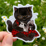 A mystery at the movies? This little black cat can't wait to see how Tuxedo, the famed feline detective, cracks this case!


This 2.5" die-cut gloss vinyl sticker is durable, weatherproof, and perfect for water bottles, notebooks, laptops, bikes, and all sorts of other surfaces! Make sure to clean and dry the surface thoroughly before applying.