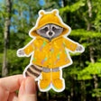 This weatherproof vinyl sticker features my illustration of a raccoon dressed up in banana slug rain gear.