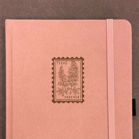Archer and Olive A5 Notebook - Texas Forever

A charming pink journal featuring a Texas bluebonnet forever stamp on the cover — a sweet nod to the Lone Star State and a perfect keepsake for writers, travelers, and stationery lovers.

✨ Features You’ll Love

Ultra-thick paper designed to prevent ghosting and bleeding

Elastic closure to keep pages secure

Built-in pen loop for your favorite pen or pencil

📓 Notebook Details

Size: A5&nbsp;

Pages:&nbsp;118 pages

Paper:&nbsp;160gsm ultra-thick, bleed-resist