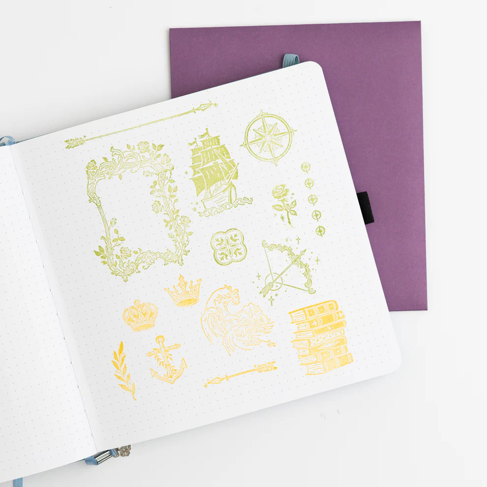 Add enchanted details to your pages with the Enchanted Chapters Stamp Set. Featuring books, ships arrows, anchors, and crowns, these reusable clear acrylic stamps are perfect for layering creative designs in your journal, planner, or scrapbook.