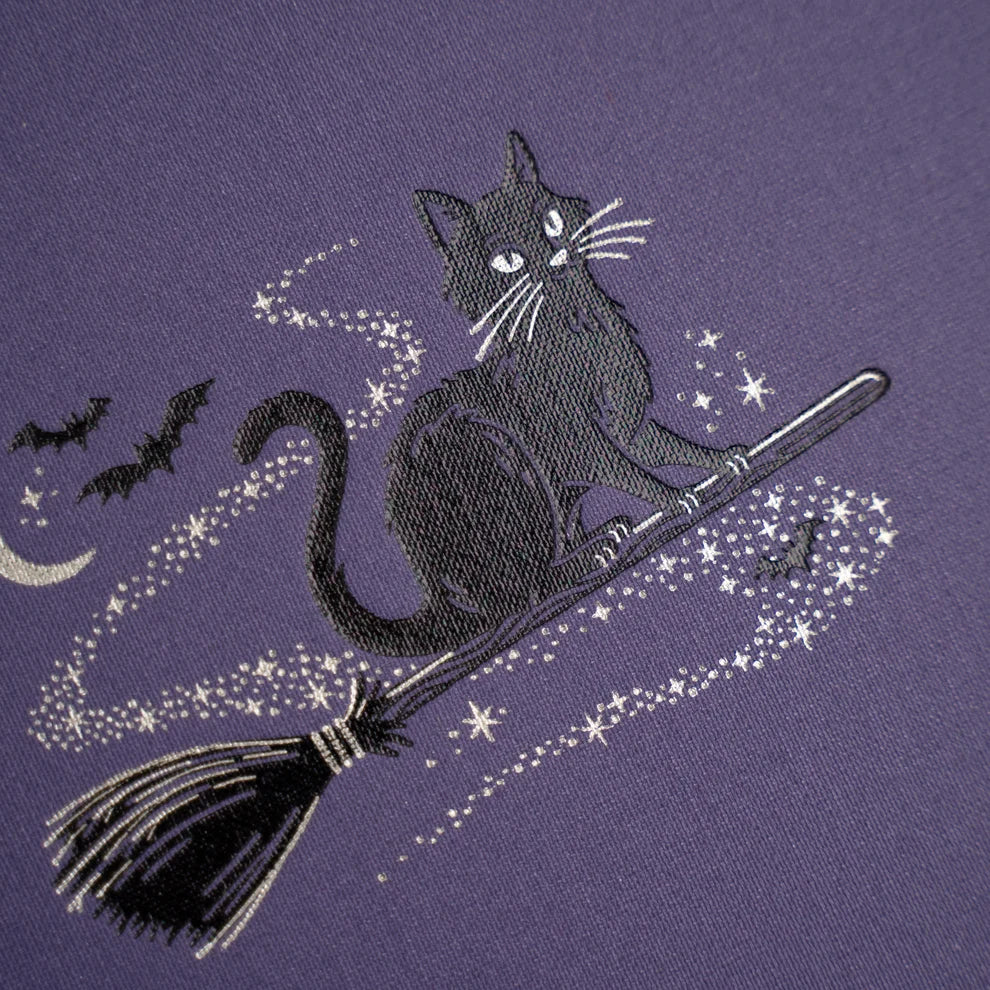 The Bewitched Notebook captures the playful spirit of Halloween with a charming black cat perched atop a broomstick beneath a crescent moon, surrounded by twinkling stars and fluttering bats.