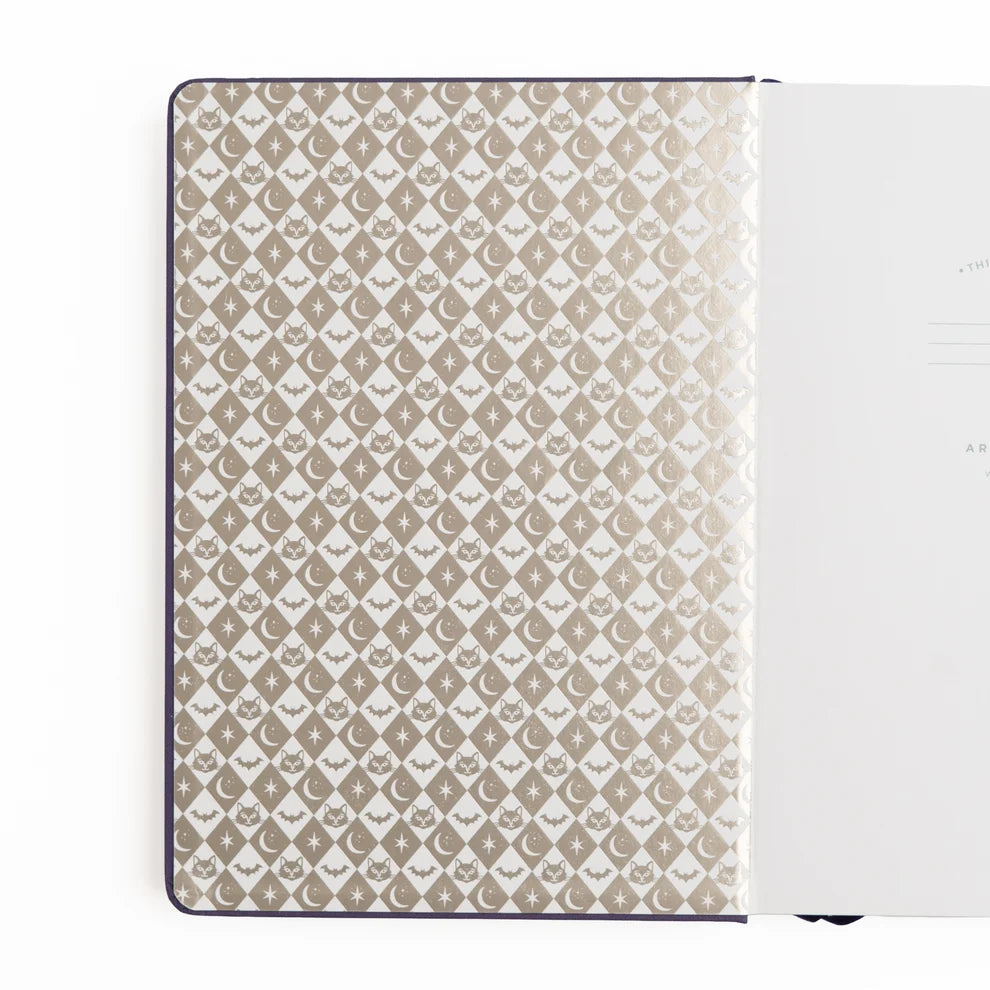 The Bewitched Notebook captures the playful spirit of Halloween with a charming black cat perched atop a broomstick beneath a crescent moon, surrounded by twinkling stars and fluttering bats.