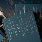 Quiet, expansive, and full of wonder — the Meteor Shower Notebook captures the magic of watching the night sky come alive. A deep, moody cover is scattered with delicate shooting stars, creating a sense of calm movement and cosmic possibility. It’s a notebook made for late-night thoughts, creative sparks, and ideas that arrive like falling stars.