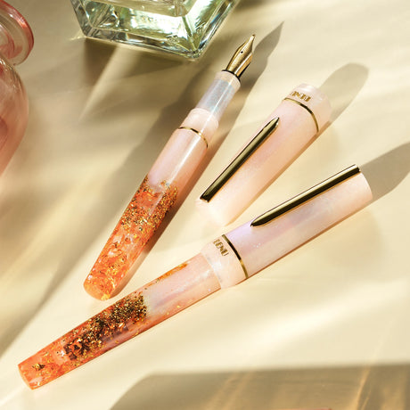BENU presents the newest Haute Collection — a line of elegant, fashion-inspired pens that blend classic charm with bold, modern flair. The designs include both subtle and vibrant styles, showcasing BENU’s signature glitter and color artistry. Each pen features a faceted body with alternating wide and slender facets, complemented by either gold-plated or chrome-plated trims for a sleek, timeless look.

A mix of golden flakes dances through a soft, pearly pink base, complemented by gleaming gold trim. Tender 