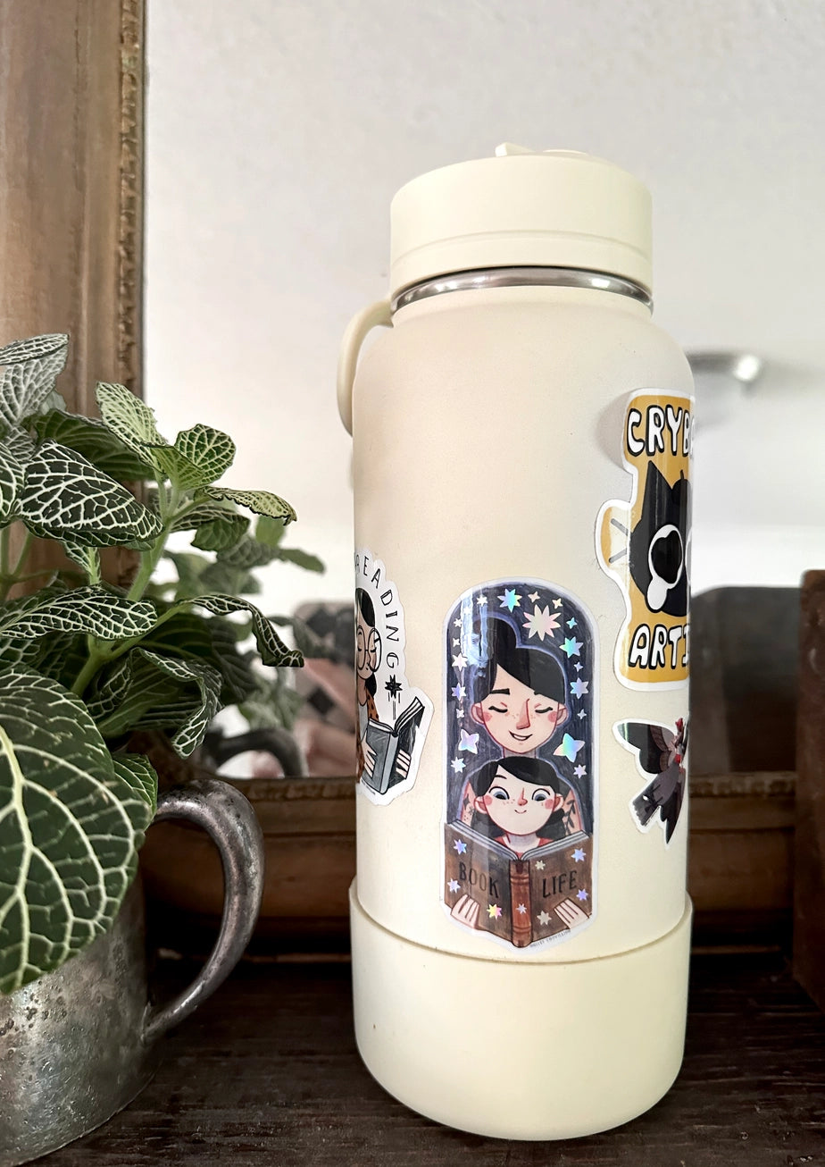 Bring the magic of storytime to life with our enchanting Mom and Kid Reading Sticker! Crafted with love and attention to detail, this holographic vinyl sticker captures a heartwarming scene of a mom and child engrossed in a book together that your customers will love!&nbsp;

Features: Size: 3.5 inches tall, 1.5 inches wide

Material: Premium vinyl with a captivating holographic finish