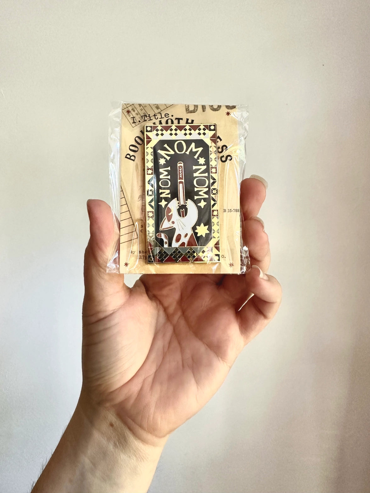 This design is part of my Book Worm Idiom Series. Book Swallower is found in Swedish and Welsh (Or so my research told me) and this design is so intricate! It has dark academia / cottage core vibes and is an adorable cat swallowing a book!&nbsp;

2.65 inches tall, gold metal lapel pin with "hard" enamel colors. Black rubber clasps. Packaged in a small plastic bag with a card backing.