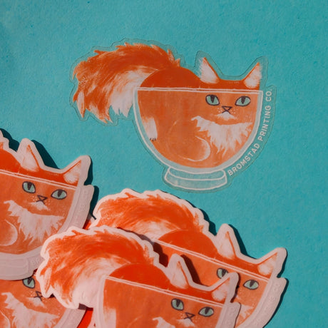 Cats are liquid, we know this. An orange boy has made himself comfy inside a clear glass bowl, fluffy tail and ears protruding. This 3" clear matte sticker is purrfect for adorning water bottles, laptops, and more. The white lines on the clear sticker pop on colorful backgrounds.