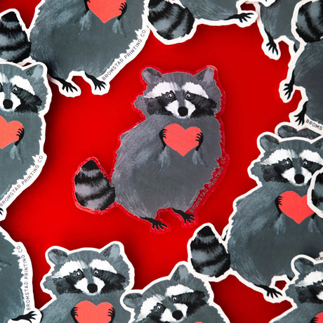 Who can resist a cute little trash panda, and one clutching a little red heart no less! This raccoon has clearly stolen yours. This 3" clear sticker is transparent around the edges of the image and ideal for adorning water bottles, laptops, and more.