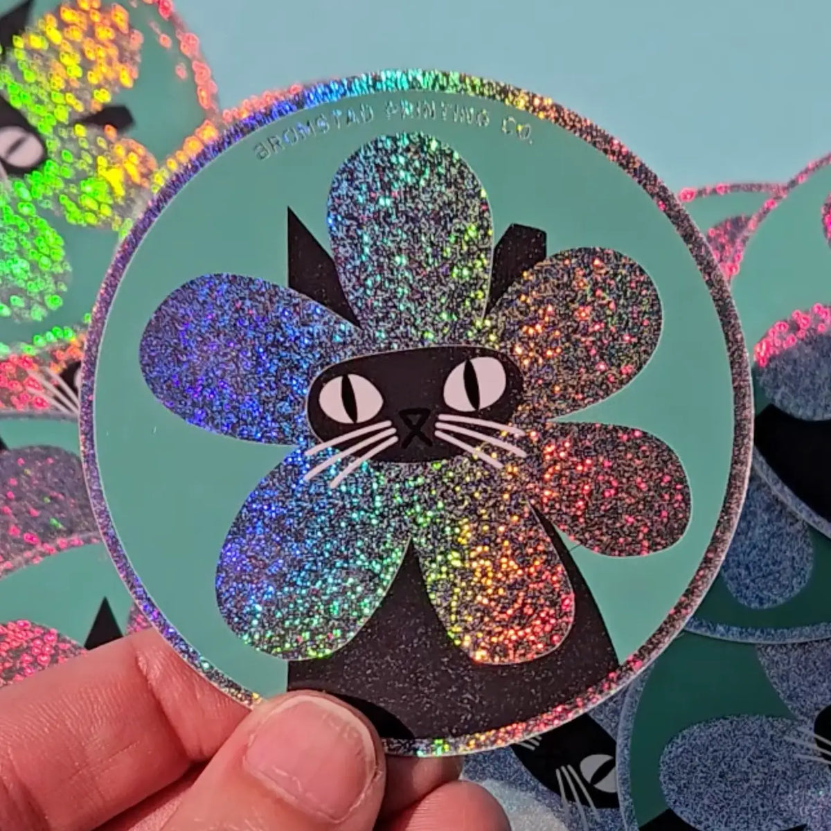 Product description
A black cat with a clipped ear wears a sparkly flower around their face. Truly, the rarest bloom. This 3" super sparkly glitter sticker is purrfect for adorning water bottles, laptops, and more. Watch how it catches the light!